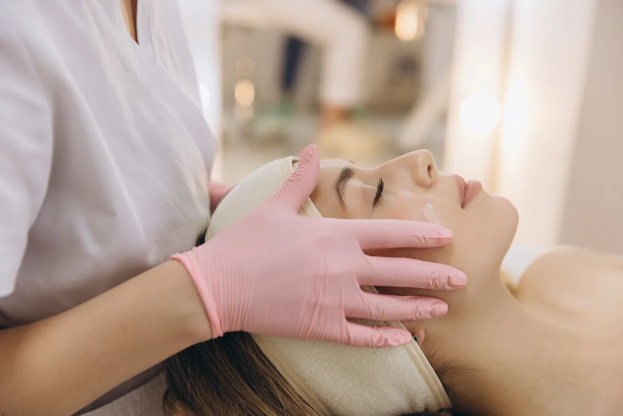 Professional cosmetologist performing facial massage with moisturizing cream on female client in beauty salon for healthy skin and rejuvenation